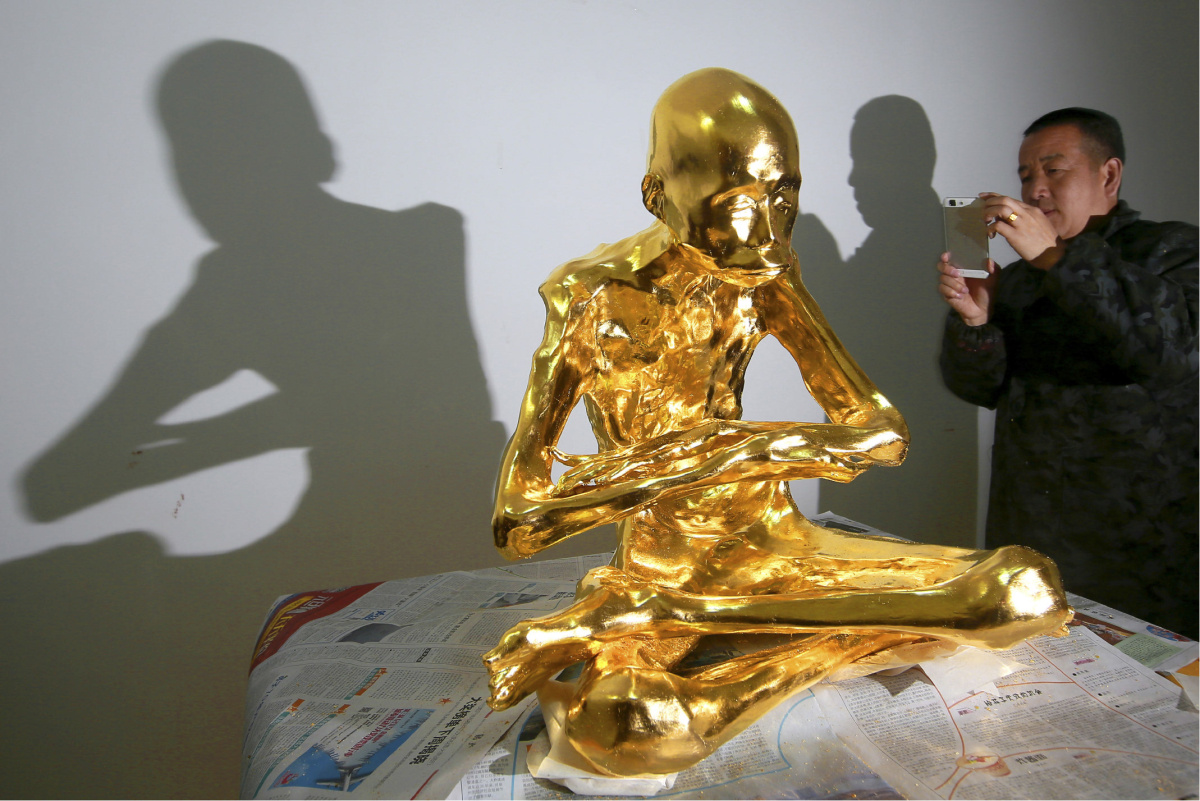 In this photo taken March 16, 2016, a man takes a photo of the mummified body of revered Buddhist monk Fu Hou in Quanzhou city in southeastern China's Fujian province. The monk, who died in 2012 at the age of 94, was prepared for mummification by his temple to commemorate his devotion to Buddhism. The mummifed remains were then treated and covered in gold leaf, a practice reserved for holy men in some areas with strong Buddhist traditions. (Chinatopix via AP) CHINA OUT