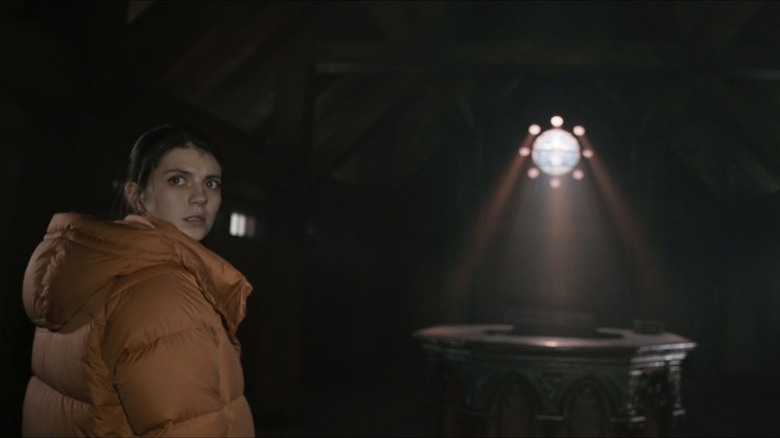 Margot se uită la camera în Paranormal Activity: Next of Kin în timp ce lumina pătrunde într-o cameră întunecată din spatele ei