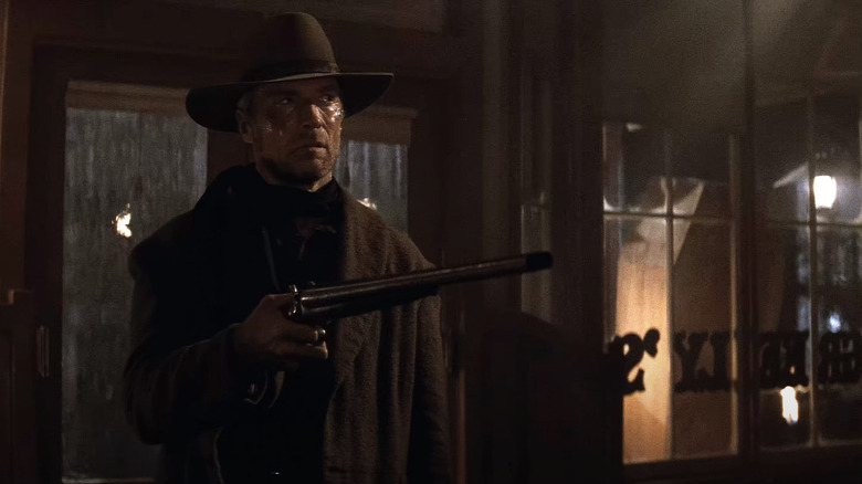 William Munny stă într-un bar ținând în sus o armă lungă
