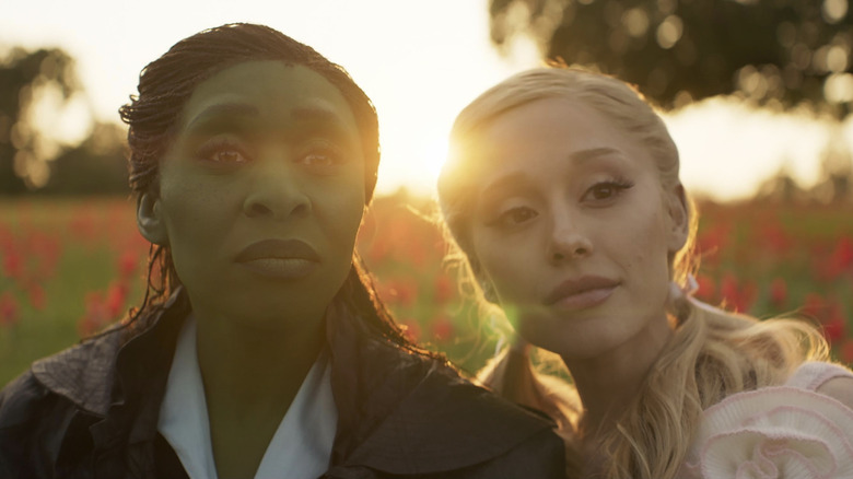 Cynthia Erivo și Ariana Grande ca Elphaba și Glinda în Wicked, stând pe un câmp de flori roșii de mac în timp ce soarele apune în spatele lor