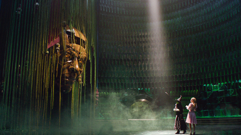 Cynthia Erivo ca Elphaba și Ariana Grande ca Glinda se confruntă cu fața mașinii Vrăjitorului în Wicked