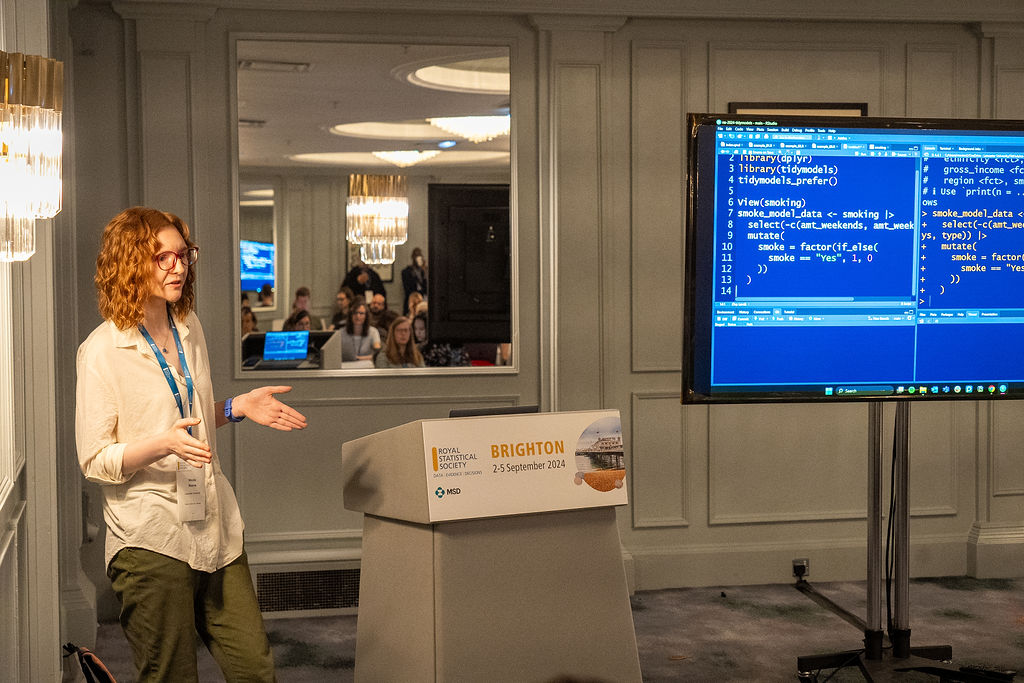 Fotografie cu mine la conferința RSS stând în fața unui televizor care arată un cod R