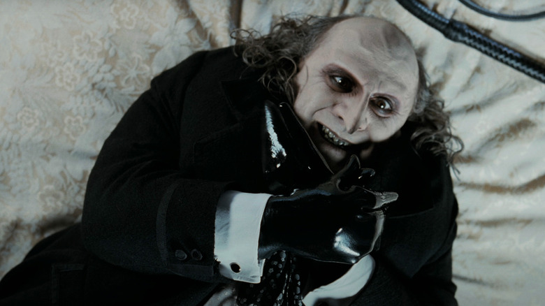 Pinguinul lui Danny DeVito stă întins pe un pat făcând o pasăre cu mâinile în Batman Returns