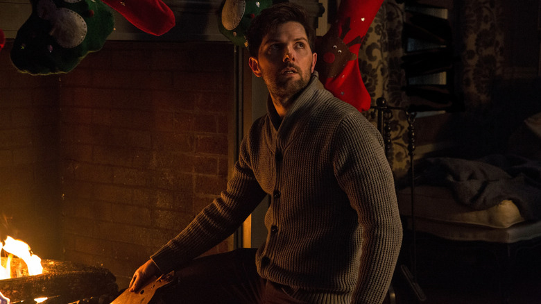 Tom, interpretat de Adam Scott, trăgând la un șemineu de Crăciun, privind peste umăr în Krampus.