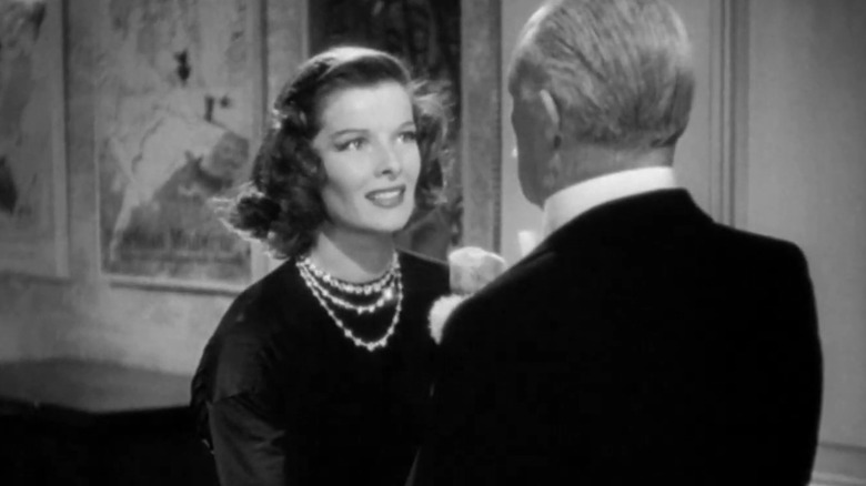 Linda de la Katharine Hepburn zâmbește în timp ce i se adresează un bărbat în vârstă care se află cu fața departe de camera în vacanță