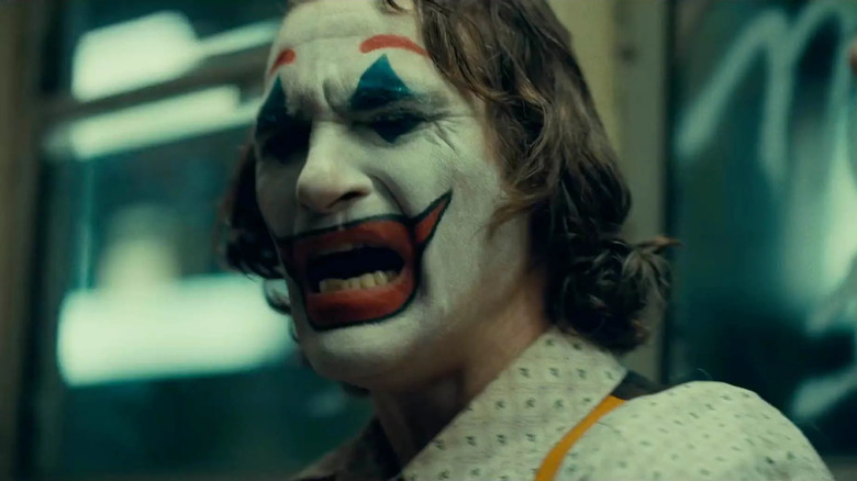 Un prim-plan cu Joaquin Phoenix ca Arthur Fleck/The Joker plângând și purtând machiaj de clovn alb, roșu și albastru în Joker