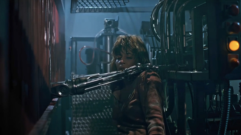 Sarah Connor din Linda Hamilton stă într-o fabrică cu brațul Terminatorului întinzându-și umărul în The Terminator