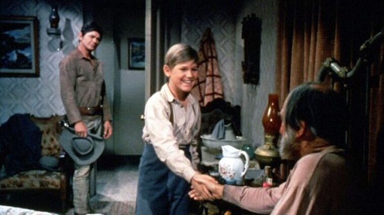 Kurt Russell în rolul lui Jamie McPheeters strânge mâna unui bătrân în timp ce Charles Bronson în rolul lui Linc Murdock se uită la Guns of Diablo