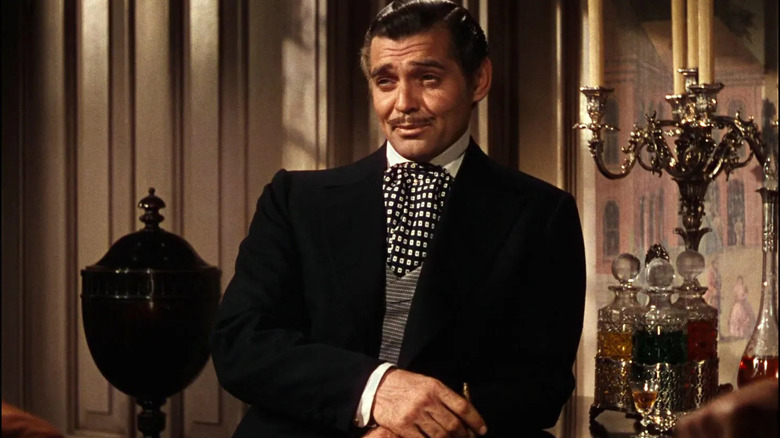 Rhett Butler, în costum, stând lângă o tavă cu sticle de băutură.