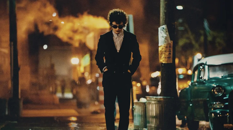Bob Dylan de la Timothée Chalamet merge pe o stradă din New York purtând un costum și nuanțe într -un necunoscut complet