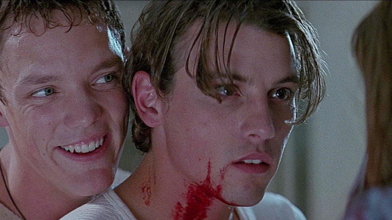 Matthew Lillard în timp ce Stu Macher zâmbește stând în spatele unui Skeet Skeet Ulrich ca Billy Loomis în Scream (1996)