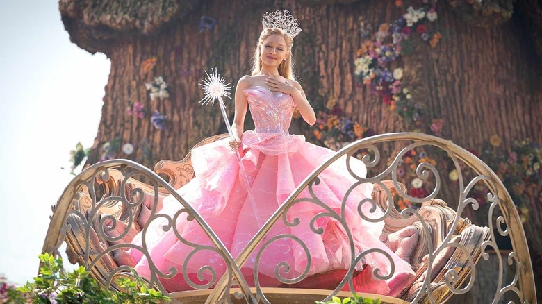 Glinda cu mâna pe inimă privind în jos la Munchkins din Wicked: Part One