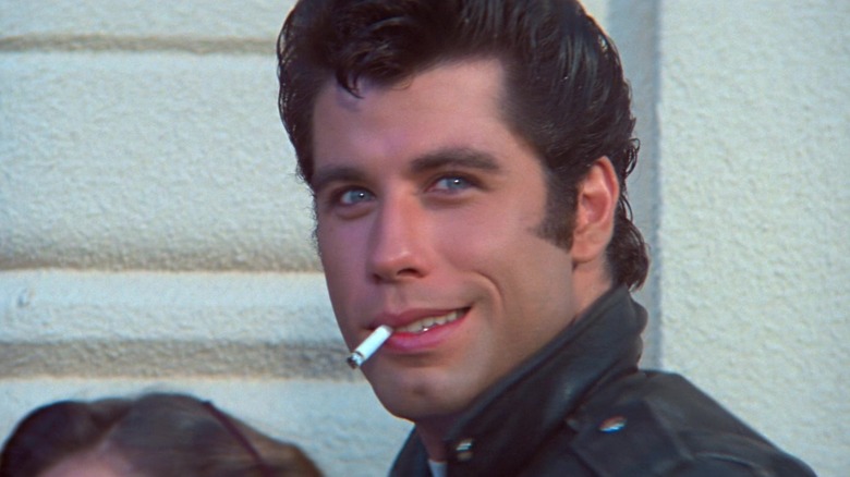 John Travolta în rolul lui Danny Zuko zâmbind cu o țigară care -și iese din gură în grăsime