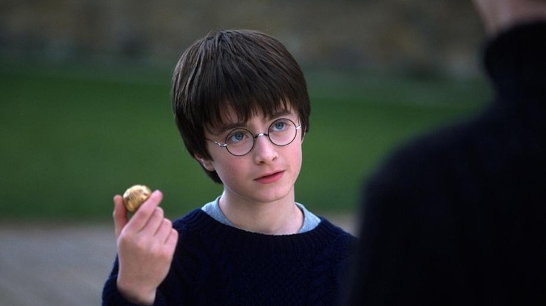 Harry ținând un snitch auriu cu ochi extrem de albaștri în Harry Potter și Piatra Vrăjitorului