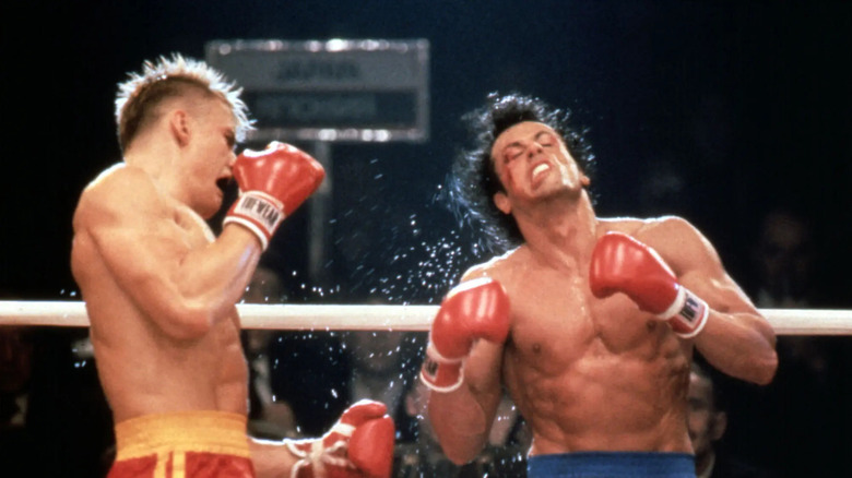 Ivan Drago (Dolph Lundgren) stă în profil, ridicându -și mănușile de box după ce a aterizat un pumn puternic pe Rocky Balboa (Sylvester Stallone), care se apleacă înapoi, trântind în durere în Rocky IV