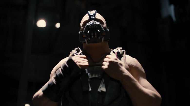 Bane -ul lui Tom Hardy își sprijină mâinile pe curelele de vestă în The Dark Knight Rises