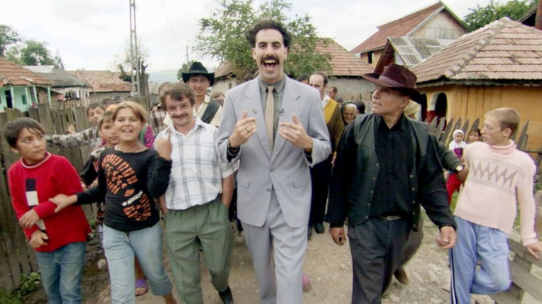 Borat în Kazahstan, mergând alături de mai mulți cetățeni, zâmbind. O scenă din Borat! Învățările culturale ale Americii fac beneficii glorioase națiune din Kazahstan.
