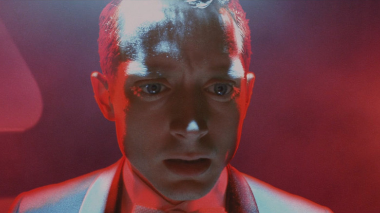 Elijah Wood ca Tom Selznick, scăldat în lumină roșie, arătând îngrozit la pianul grandios