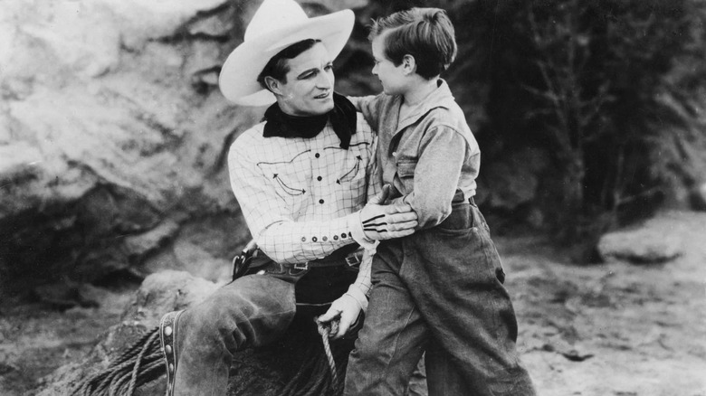 Tom, în cowboy -ul său plin, mângâind un băiat tânăr în filmul din 1926 No Man's Gold.