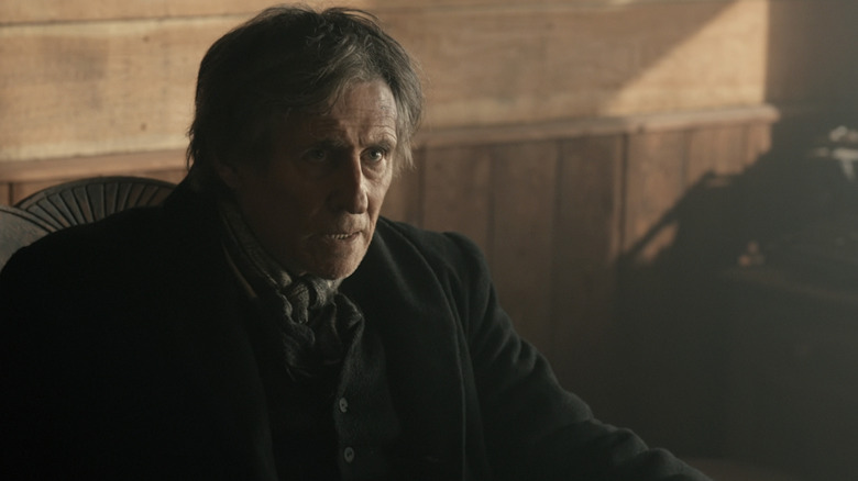 Șeriful lui Gabriel Byrne, Jim Ambrose, se uită în sus în timp ce stă pe un scaun din Muder din Yellowstone City