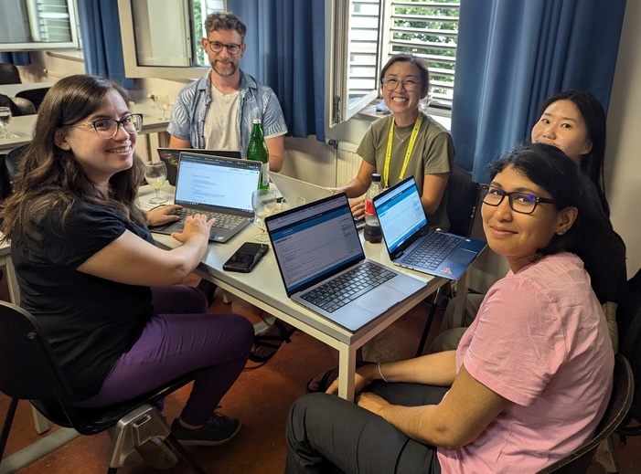 Participanții care stau în jurul unui birou cu laptopurile lor într -o zi R Dev, întorcându -se să zâmbească la aparatul foto. Grupul pare a fi predominant femei de naționalități multiple, iar unul dintre grupuri poate fi recunoscut drept cunoscutul dezvoltator R, Hadley Wickham.