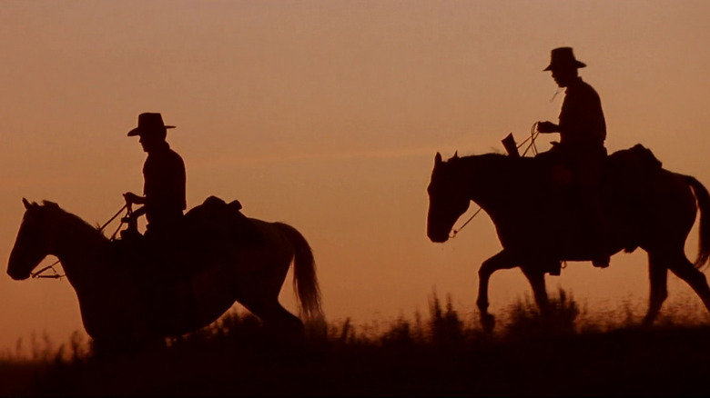 Siluetele a doi cowboy pe cal în neiertare