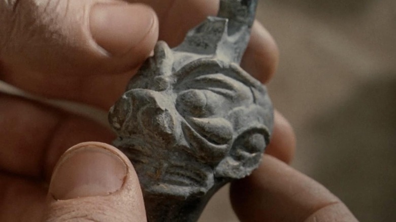 Un cap mic de demon de piatră, ținut în degete, în apropiere. Din exorcist.