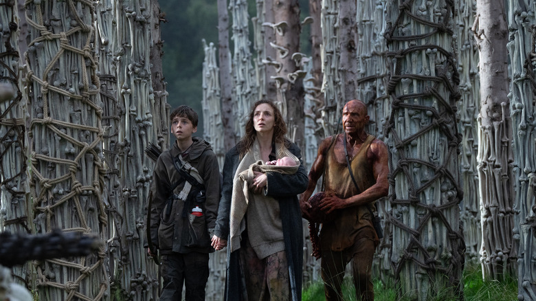 Spike, Isla (ținând un copil) și Dr. Ian Kelson stând printre multe oase în 28 de ani mai târziu