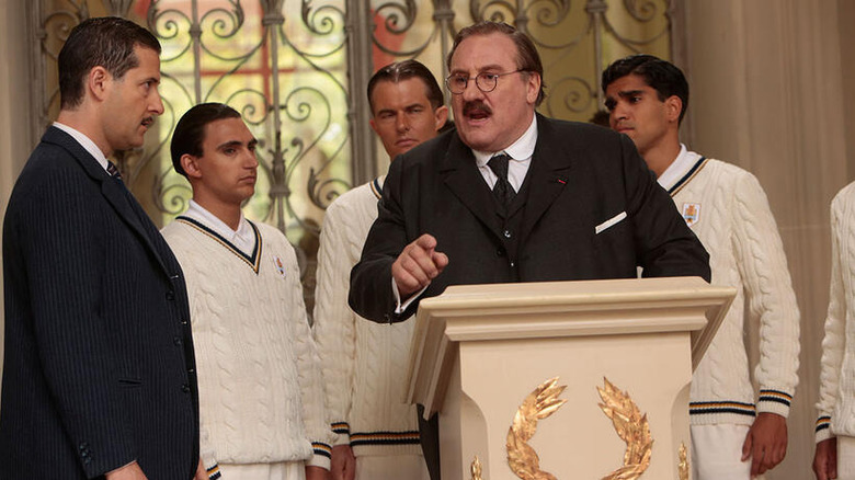 Jules Rimet pe un podium, fotbaliști în spatele lui, în United Passions