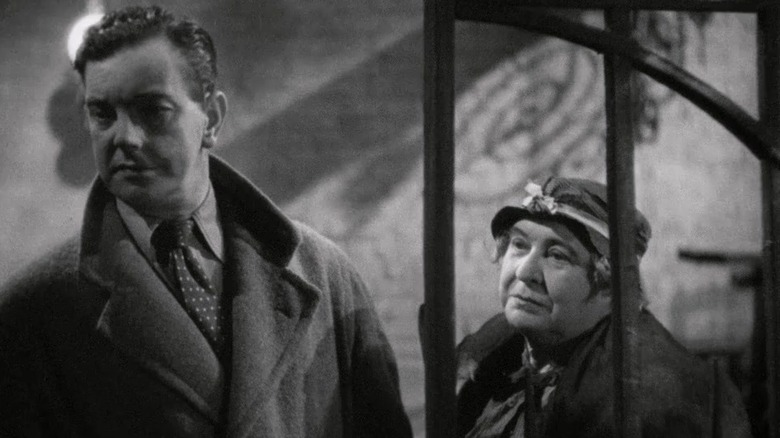 Leslie Banks în rolul lui Bob Lawrence și Clare salută ca doamna Brockett stând împreună la omul care știa prea puțin