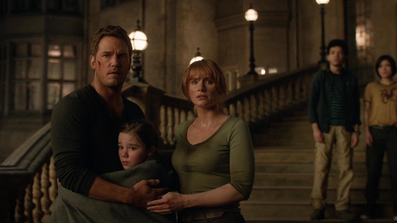 Owen și Claire îl îmbrățișează pe Charlotte în timp ce se uită în șoc din afara unui conac din Jurassic World: Dominion