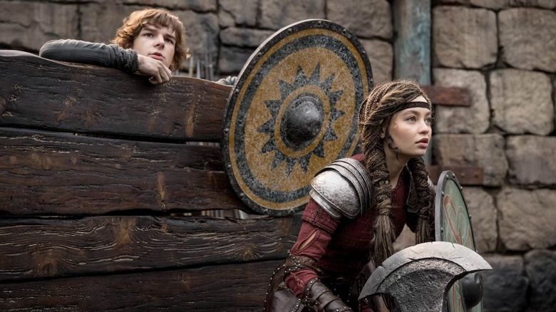 Sughiț ascunzându -se în spatele unui gard cu Astrid în față, ținând un scut în modul de a -ți antrena dragonul