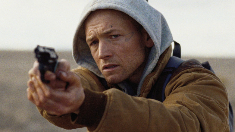 Ea merge cu pușca - Nate (Taron Egerton) care ține un revolver