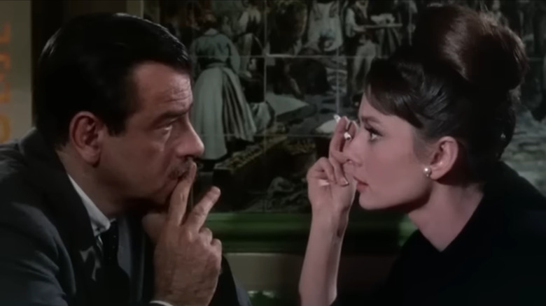 Charade, Brian vorbind cu Reggie la o cafenea, Reggie fumând o țigară