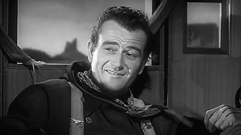 John Wayne ca Henry, copilul Ringo, zâmbește în timp ce stă în stagecoach în Stagecoach