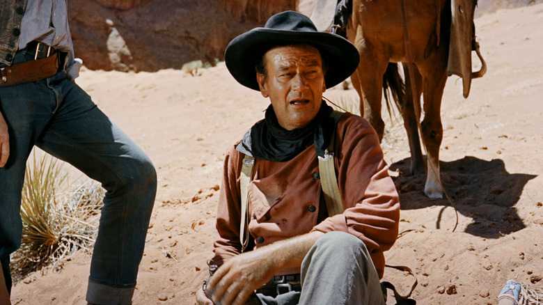 John Wayne ca Ethan Edwards stă deținând o cantină de apă în căutători