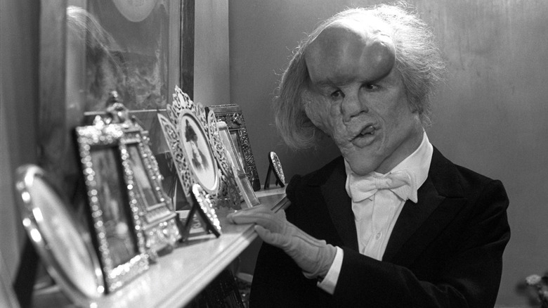 John Merrick privind o manta de fotografii încadrate în The Elephant Man