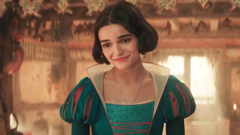 Albă ca zăpada, purtându -și rochia de ceai, zâmbește călduros cu o fereastră luminată de soare în spatele ei, în interiorul cabanei piticilor în Albă ca Zăpada și a celor șapte pitici