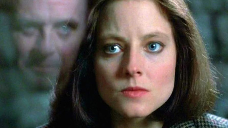 Clarice arătând intens cu reflectarea lui Hannibal Lecter în paharul de lângă ea, o scenă din tăcerea mieilor