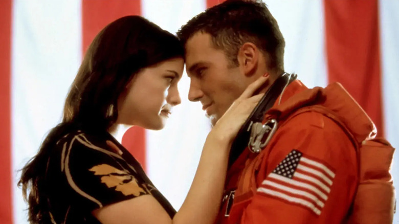 Grace (Liv Tyler) și AJ (Ben Affleck), purtând un costum de astronaut portocaliu, se aplecă să atingă fruntele în timp ce stăteau în fața unui fundal mare de steag american din Armageddon
