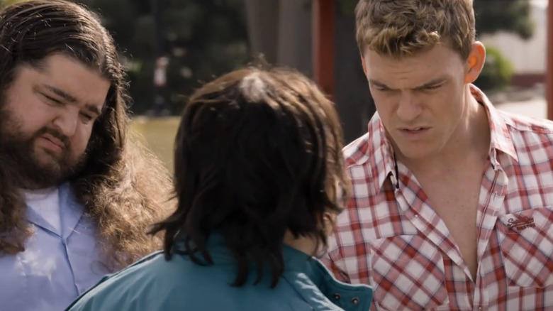 Kip Loyola/Carew al lui Alan Ritchson stă lângă Lurch/Garvey al lui Jorge Garcia în timp ce vorbesc cu cineva cu spatele la aparatul foto în soneria de nuntă