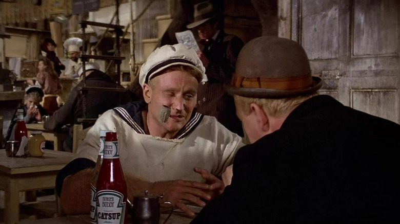Popeye cu o țeavă stând peste o masă de la Wimpy în Popeye