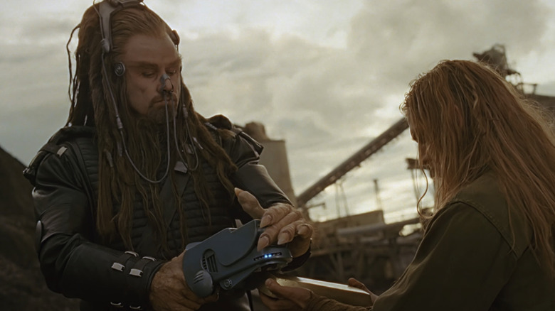 Terl -ul lui John Travolta se uită în jos în timp ce ține un dispozitiv în Battlefield Earth