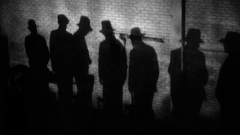 Umbrele mai multor oameni care poartă pălării pe un perete de cărămidă din Scarface (1932)