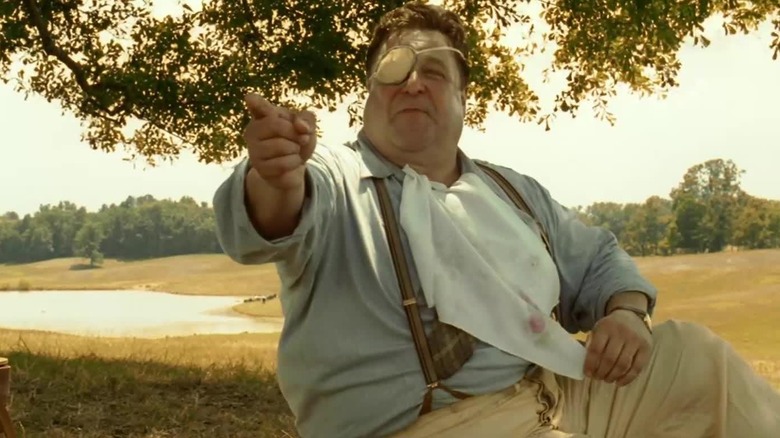 John Goodman în rolul lui Big Dan Teague, Cyclops, arătând pe cineva de pe ecran și zâmbind în O frate, unde ești?