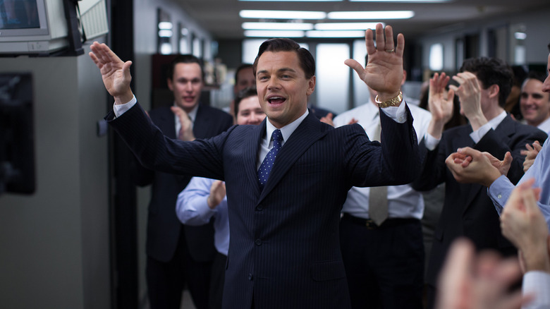 Leonardo DiCaprio în rolul lui Jordan Belfort purtând un costum și ținându -și mâinile în fața unei mulțimi aplaudate în lupul Wall Street