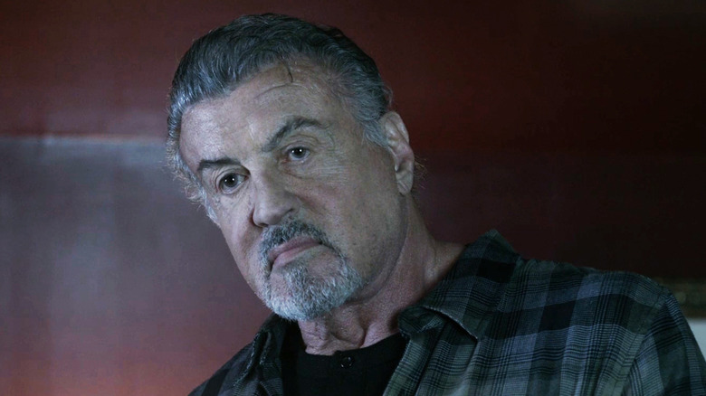 Sylvester Stallone în calitate de agent Chester care stă pe un perete roșu din Alarum