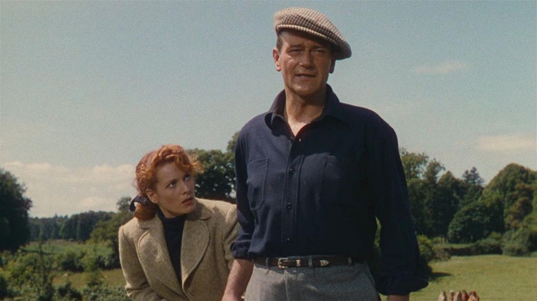 Maureen O'Hara ca Mary Kate Danaher și John Wayne în rolul lui Sean Thornton stând pe un câmp în The Quiet Man