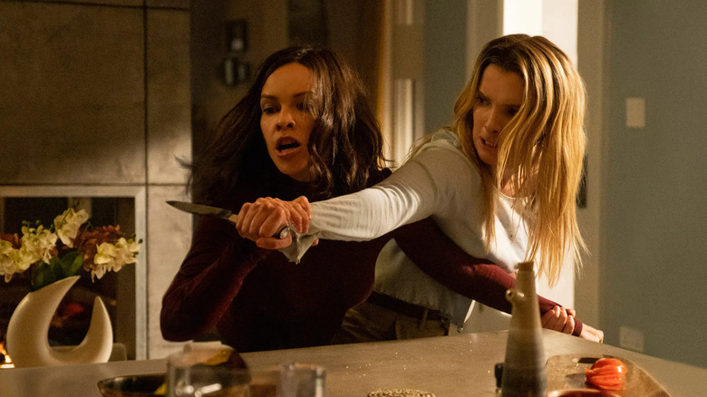 Athena (Hilary Swank) apucă brațul lui Crystal (Betty Gilpin) și mâna ținând un cuțit, ambele purtând expresii intense în vânătoare