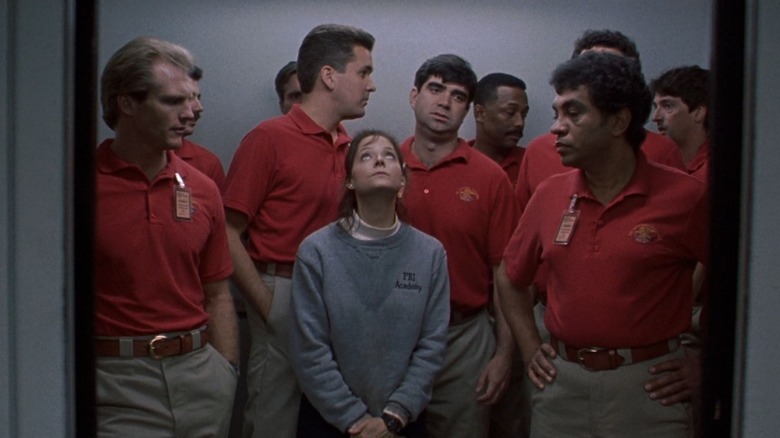 Jodie Foster în timp ce Clarice Starling in the Silence of the Lambs stând în liftul FBI înconjurător de agenți masculi în cămăși roșii